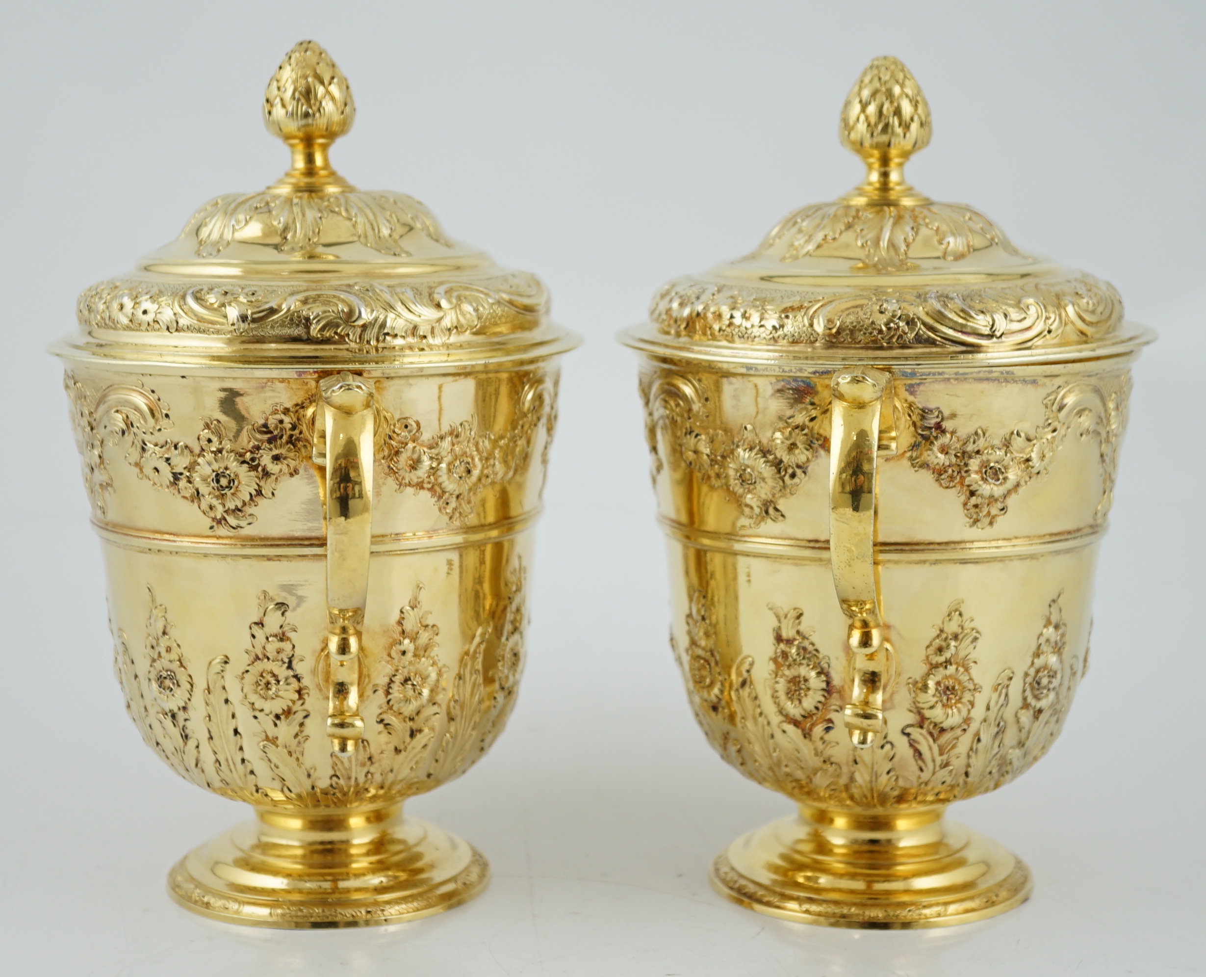 Benacre Hall, Suffolk. A good pair of George II embossed silver gilt two handled pedestal cups and covers, by Benjamin Gignac